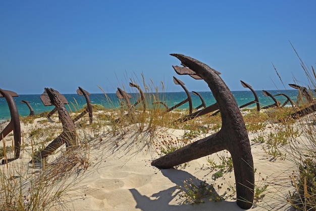 Rostige metallische Anker im Sand am Strand vor klarem Himmel