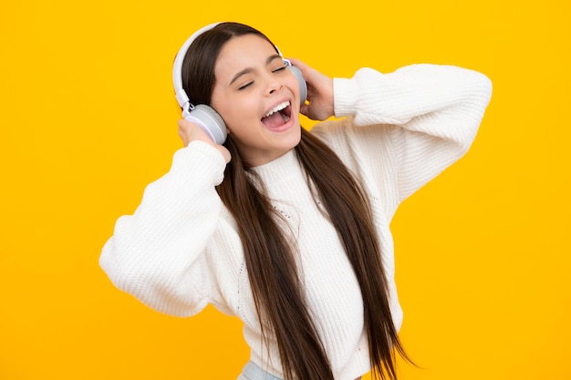 Rosto animado Adolescente em fones de ouvido sem fio modernos curtindo música no aplicativo de áudio ouvindo sua música favorita sobre fundo amarelo do estúdio Expressão espantada alegre e feliz