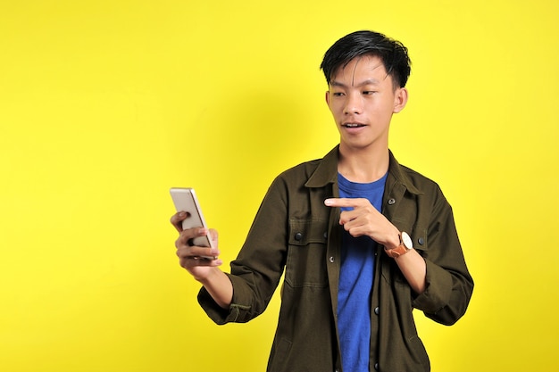 Rosto chocado de um homem asiático de camisa branca, olhando para a tela do telefone em fundo amarelo.