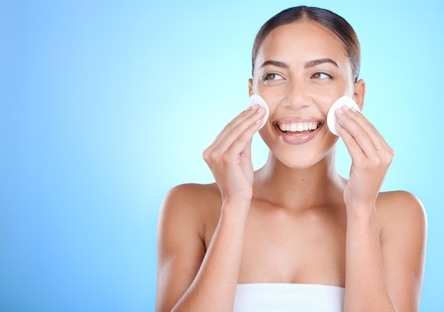 Rosto de cuidados com a pele e mulher com almofadas de algodão cosméticos e bem-estar no fundo azul do estúdio Removedor de maquiagem feminina e mexicana com sorriso beleza natural e confiante para uma pele clara e lisa