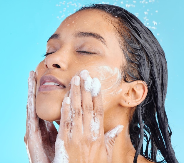 Foto rosto de espuma de banho e limpeza de mulher negra com líquido de água para hidratação sabonete de saúde de beleza ou higiene para a pele estúdio de autocuidado spa salão e modelo de relaxamento lavando isolado em fundo azul