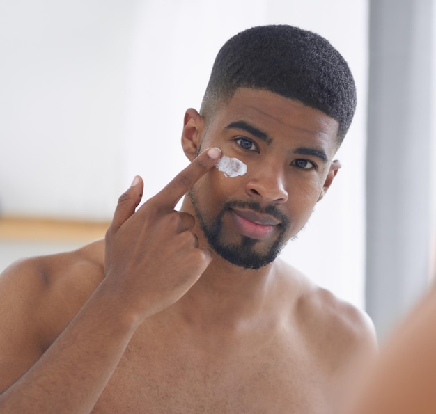 Foto rosto de homem e beleza com espelho e cuidados com a pele com creme e higiene durante a rotina matinal em casa indivíduo do sexo masculino em retrato de banheiro com loção e bem-estar facial limpo e hidratante