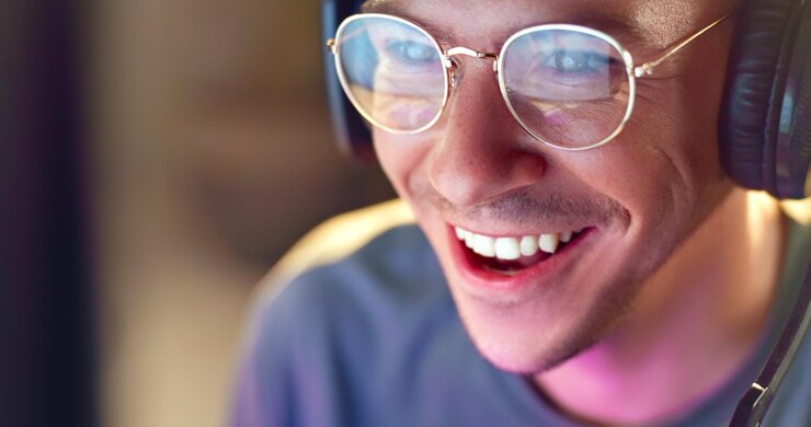 Foto rosto de homem feliz e jogador com fones de ouvido para torneio de esport online ou streaming em casa jovem homem ou streamer com sorriso ou fone de ouvido à noite para console de diversão ou jogos de computador em casa