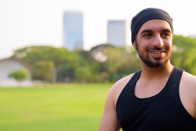 Rosto de jovem bonito e feliz indiano barbudo pensando no parque