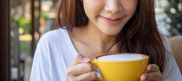 Rosto de jovem relaxante com leite quente ou café durante a manhã. Mulher bebe café em um café. boa sensação com conceito de bebida de café