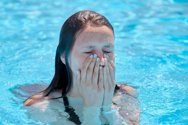 Rosto de menina em uma piscina ao ar livre, jovem enxuga o rosto com as mãos de gotas de água