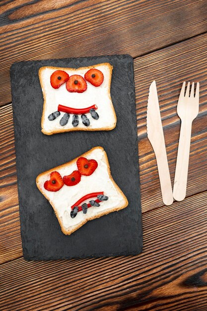 Foto rosto de monstro engraçado em halloween sanduíche pão torrado com morango de manteiga doces cortar prancha de servir em fundo preto crianças criança doce sobremesa pequeno-almoço almoço comida