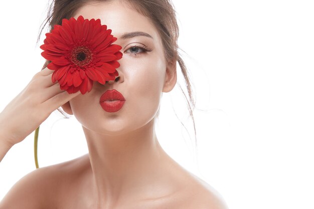 Rosto de mulher bonita com batom vermelho mandando beijos e segurando uma flor perto do olho