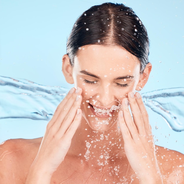 Foto rosto de mulher e cuidados com a pele com esguicho em estúdio para beleza, bem-estar e autocuidado por fundo azul modelo de água e sorriso com limpeza de hidratante e feliz por cosméticos naturais para dermatologia