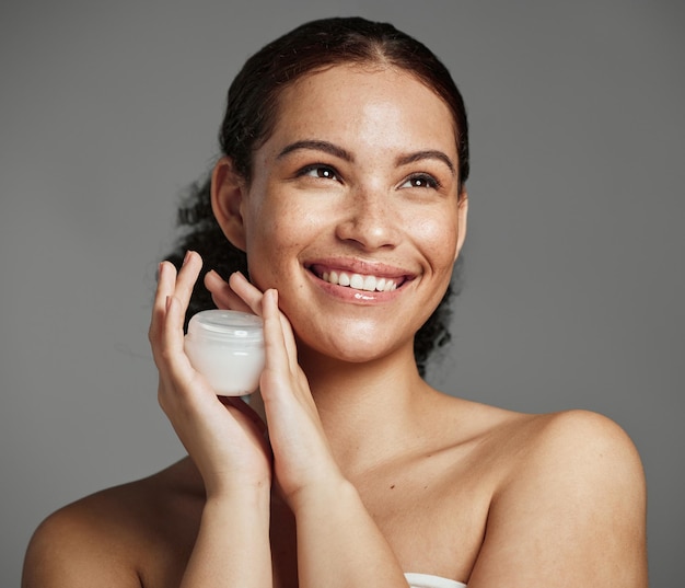 Rosto de mulher negra e recipiente de creme para a pele com brilho de beleza saudável e sardas naturais Menina cosmética de pensamento com sorriso e produto de loção facial de luxo no fundo cinza do estúdio