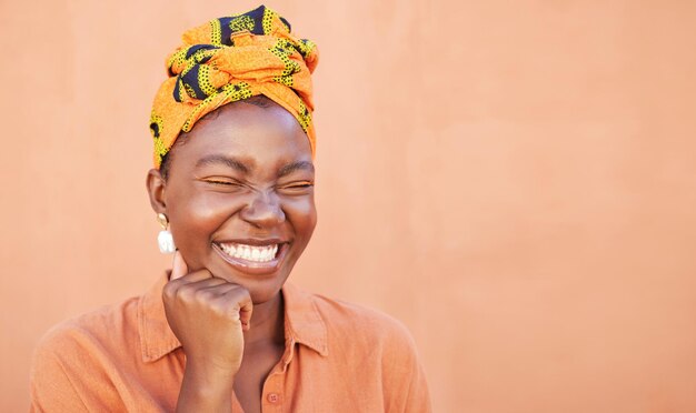 Rosto de mulher negra e sorriso com um turbante e espaço livre para a cultura africana felicidade e maquete de beleza em fundo de pêssego Mulher africana com lenço de cabeça tradicional da moda da Nigéria enquanto ria