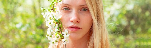 Rosto de mulher primavera para banner. Retrato de mulher bonita close-up. Mulher no fundo com flores em um dia de primavera.