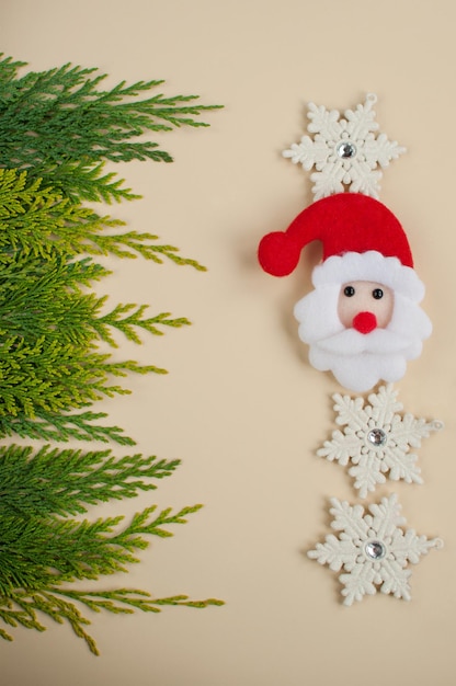 Rosto de Papai Noel de feltro no fundo de ramos verdes de thuja e decoração de flocos de neve brancos com espaço para texto em formato vertical