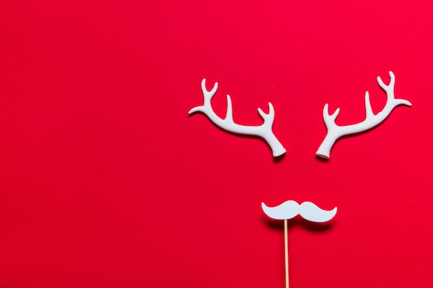 Rosto de rena festivo feito de chifres brancos e bigode branco sobre fundo vermelho