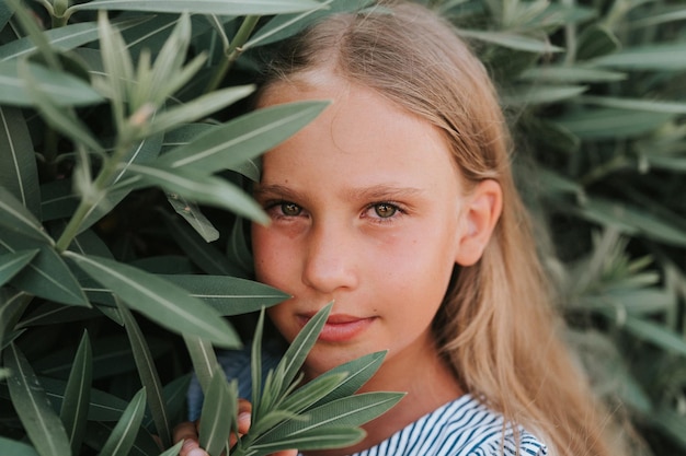 Rosto de retrato de uma garotinha feliz sincera de oito anos de idade com longos cabelos loiros e olhos verdes no fundo de plantas verdes durante um conceito de saúde mental gen z de viagem de férias de verão