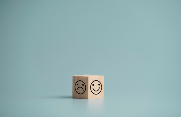 Rosto de sorriso e rosto de tristeza imprimem tela de dois lados de um bloco de cubos de madeira sobre fundo azul