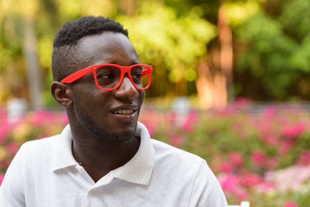 Rosto de um jovem africano feliz com óculos pensando ao ar livre no parque