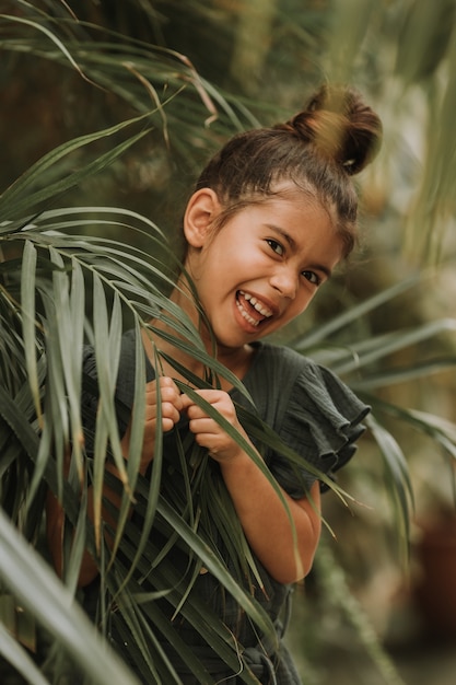 Foto rosto de uma menina cercada de folhas tropicais. retrato de um lindo bebê moreno