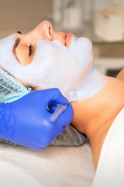 Foto rosto descascando na esteticista. tratamento facial. a esteticista aplica uma máscara facial de limpeza na paciente do sexo feminino.