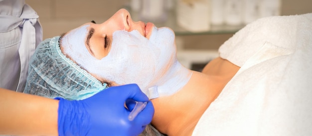 Foto rosto descascando na esteticista. tratamento facial. a esteticista aplica uma máscara facial de limpeza na paciente do sexo feminino.