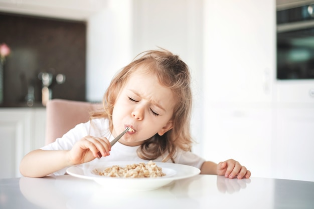 Rosto emocional com fome e desfrutar de comer o conceito. Pequeno-almoço saboroso e comida deliciosa. Menina, desfrutando de uma tigela de cereal. Desfrutando de comer comida saborosa no café da manhã na cozinha.