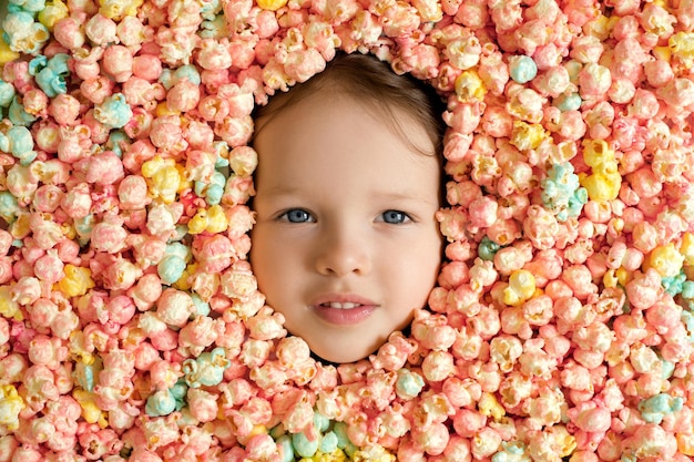 Rosto sério de uma criança cercada por uma grande pilha de pipoca multicolorida