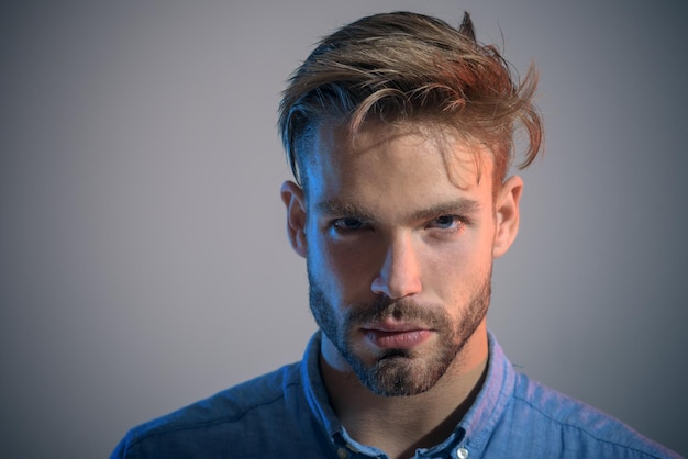 Rosto sério do retrato de homem. Conceito de negócio, educação e escritório - retrato da moda do empresário bonito barbudo. Homem estiloso com barba por fazer, bigode e penteado moderno em camisa jeans casual