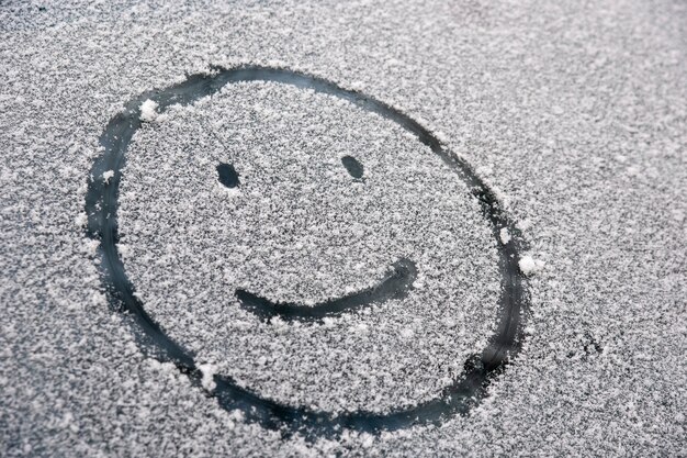 Rosto sorridente alegre pintado na janela do carro coberto de neve.