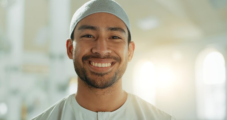 Foto rosto sorridente e homem muçulmano na mesquita em lente flare com boné de oração para adorar deus alá e louvar retrato de pessoa feliz e islâmica no templo em chapéu para fé cultura e risada engraçada nos emirados árabes unidos