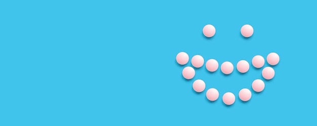 Rosto sorridente forrado com pílulas cor-de-rosa em uma vista superior de fundo azul Pílulas médicas para cuidados de saúde