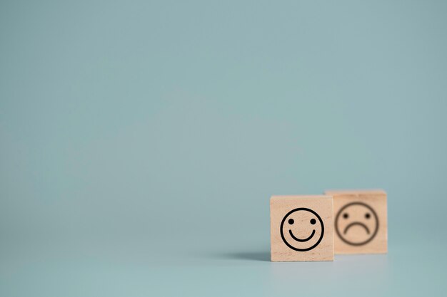 Rosto sorridente na frente do rosto de tristeza que imprime a tela em um bloco de cubo de madeira, seleção de emoção para satisfação do cliente e conceito de avaliação.
