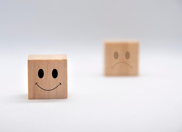 Rostos de emoticons felizes e tristes em cubos de madeira com cobertura de fundo branco Satisfação do feedback do cliente e conceito de avaliação