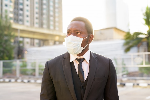 Rostro del empresario africano con máscara pensando en las calles de la ciudad