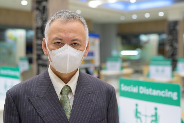 Rostro del empresario japonés maduro con máscara social distanciamiento en el patio de comidas