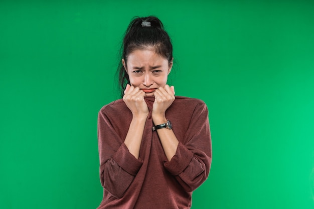 El rostro de una expresión de llanto de una joven asiática mientras sostiene su barbilla con ambas manos sobre un fondo verde