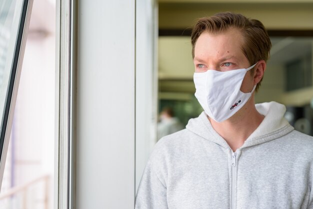 Rostro de hombre joven con máscara pensando y mirando por la ventana listo para el gimnasio