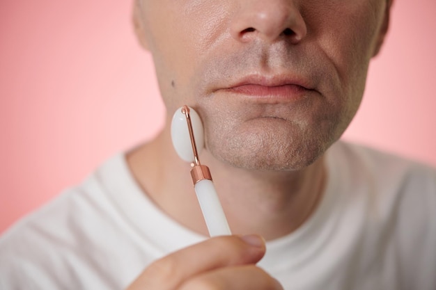 Rostro de un hombre de mediana edad masajeando el tercio inferior de su rostro con un rodillo de cuarzo