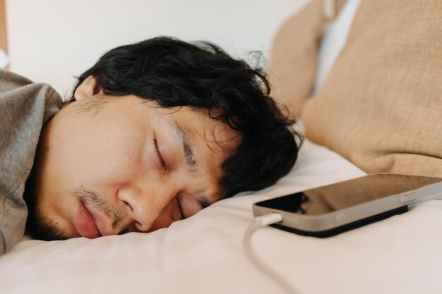El rostro de un hombre somnoliento durmió con su teléfono móvil dejado cerca de su cabeza