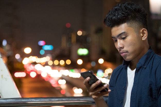 Rostro de joven asiático con teléfono en vista de la calle de la ciudad por la noche
