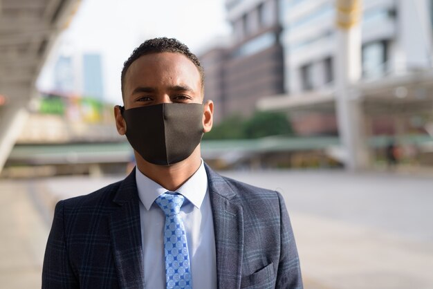 Rostro de joven empresario en traje con máscara para protegerse del brote del virus corona en la ciudad