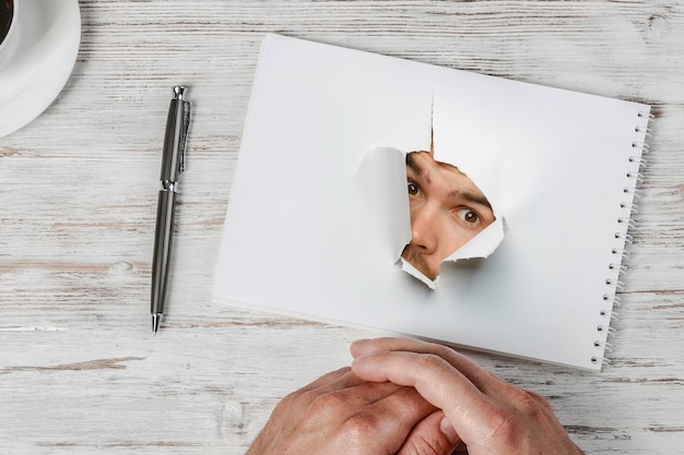 Rostro masculino a través del agujero en papel. Técnica mixta