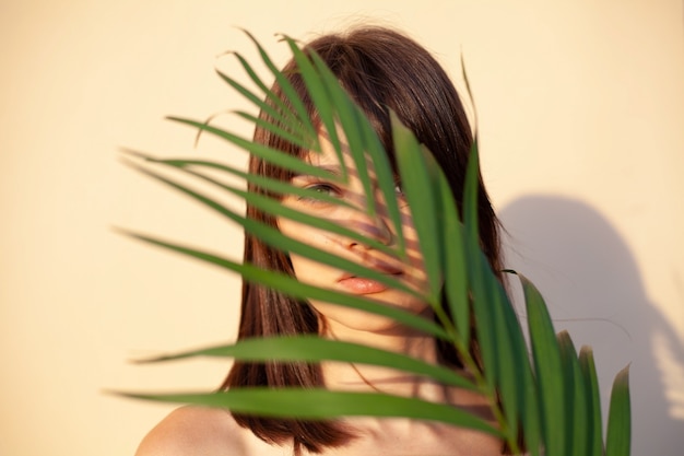 El rostro de la niña con cuadrados de cabello castaño cubiertos con una rama verde sobre fondo beige