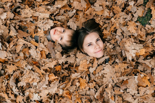 Rostros de madre e hijo entre hojas de otoño