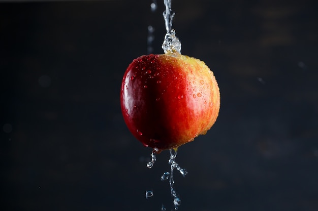 Rot-gelber großer Apfel, mit Wasser überflutet auf dunklem Hintergrund