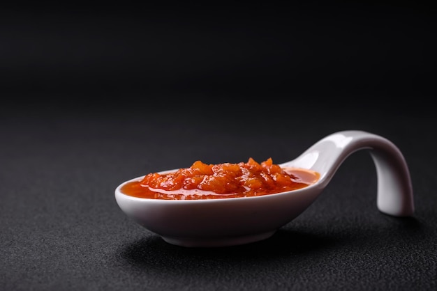 Rote Adjika-Sauce oder Ketchup mit Gewürzen und Kräutern auf dunklem Betonhintergrund