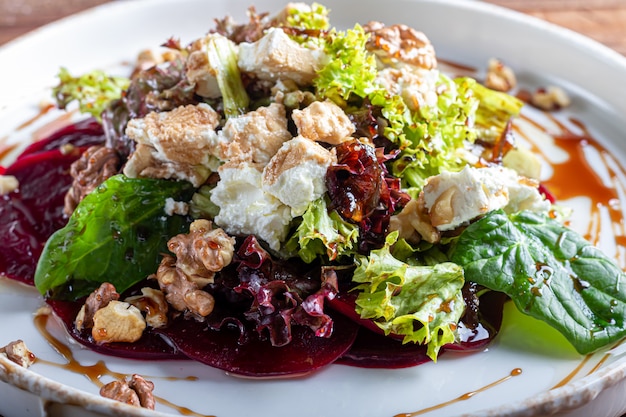 Rote-Bete-Carpaccio mit Walnüssen, Ziegenkäse, Salat und Spinat. Mit Sauce gekleidet. Auf einem dunklen Hintergrund.