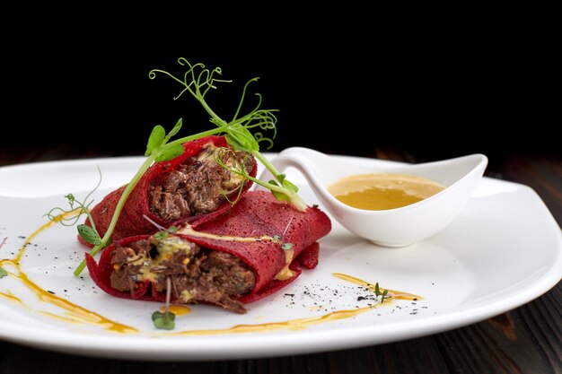 Rote-Bete-Pfannkuchen mit Fleisch, auf einem weißen Teller, auf einem Holzbrett