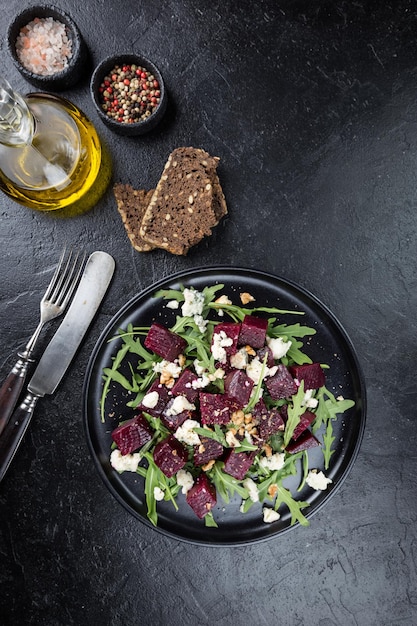 Rote-Bete-Salat mit Blauschimmelkäse, Rucola und Walnuss in einer schwarzen Platte auf Steinhintergrund, Ansicht von oben