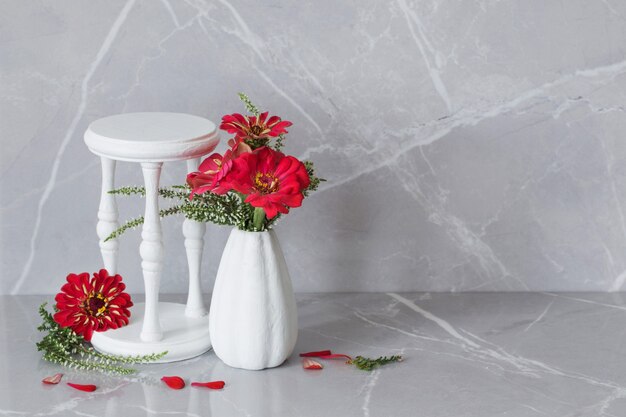 Rote Blumen in weißer Vase und Holzständer auf grauem Marmorhintergrund