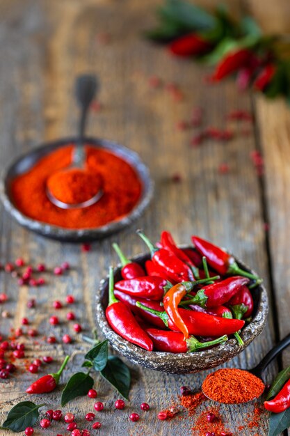 Rote Chilischoten mit einem Zweig Basilikum in einem Korb aus Weidenmetall auf einem Holztisch.